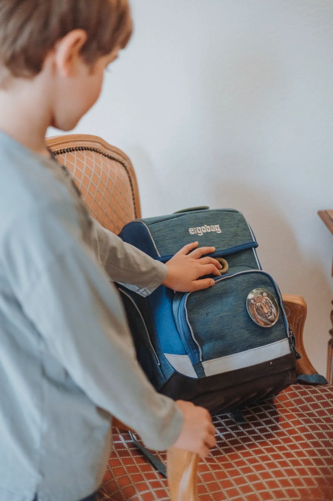 Kind räumt konzentriert seinen Schulrucksack auf einem Stuhl