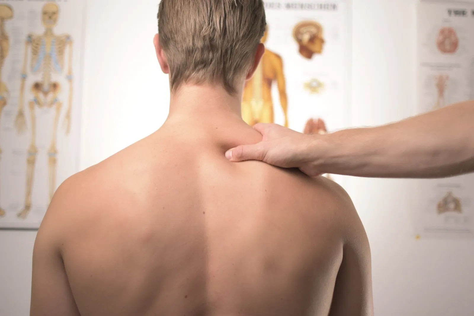 Behandelnde Hand am Nacken einer Person, im Hintergrund anatomische Lehrtafeln
