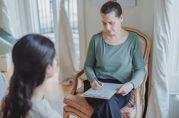 Judith Wüthrich sitzt im Behandlungszimmer der Praxis Zentral und macht sich im Gespräch mit einer Klientin Notizen