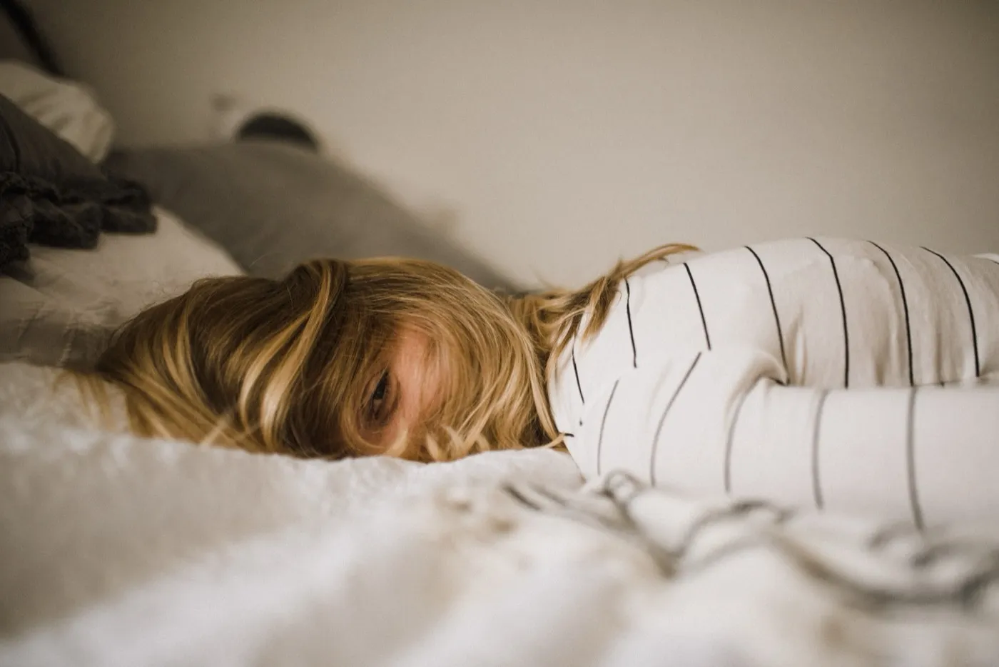 Person liegt erschöpft auf dem Bauch im Bett, das Gesicht halb im Kissen