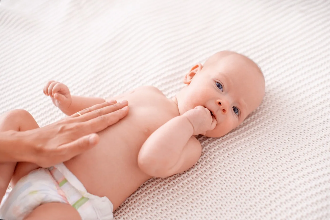Ein Baby liegt auf dem Rücken, eine Hand streicht flach über seinen Bauch
