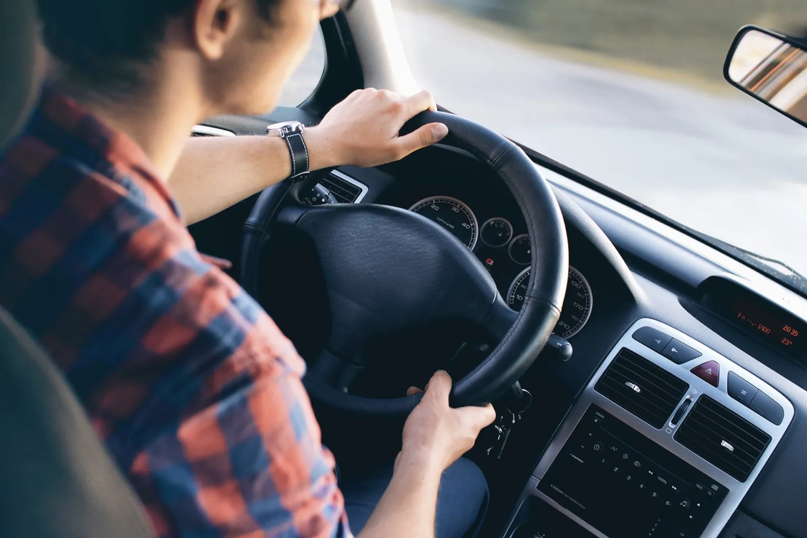 Person am Steuer eines Autos, Blick über die Schulter auf Lenkrad und Armaturenbrett