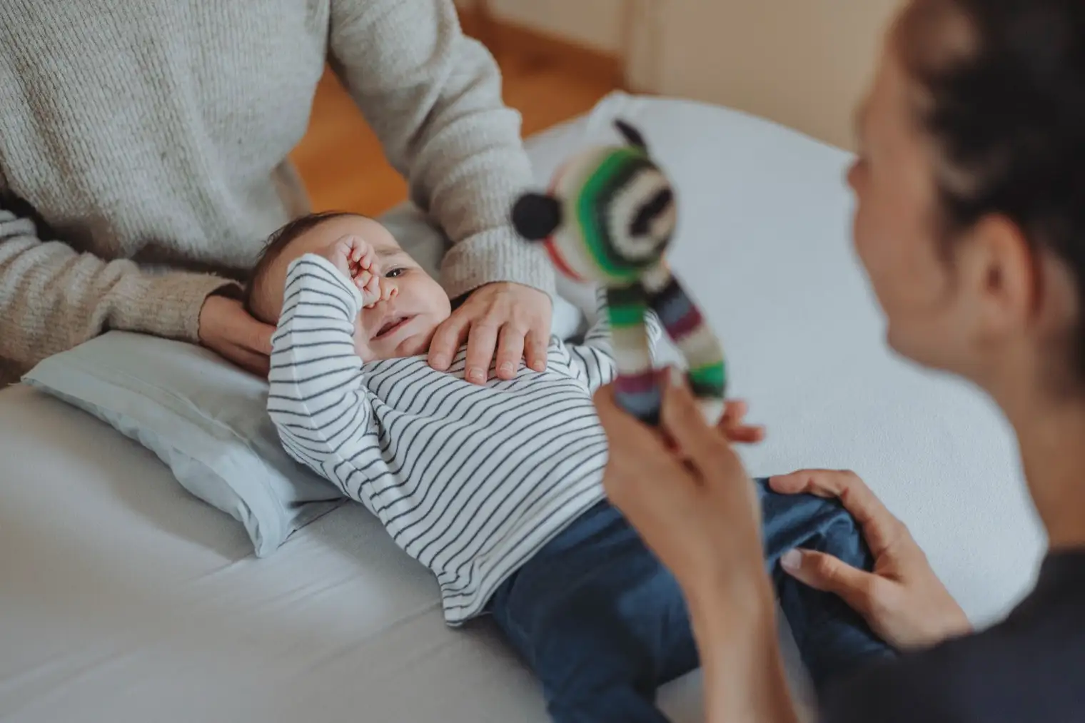 Baby liegt entspannt auf der Behandlungsliege, eine Hand ruht sanft auf seinem Brustkorb, die Mutter ist nah dabei.