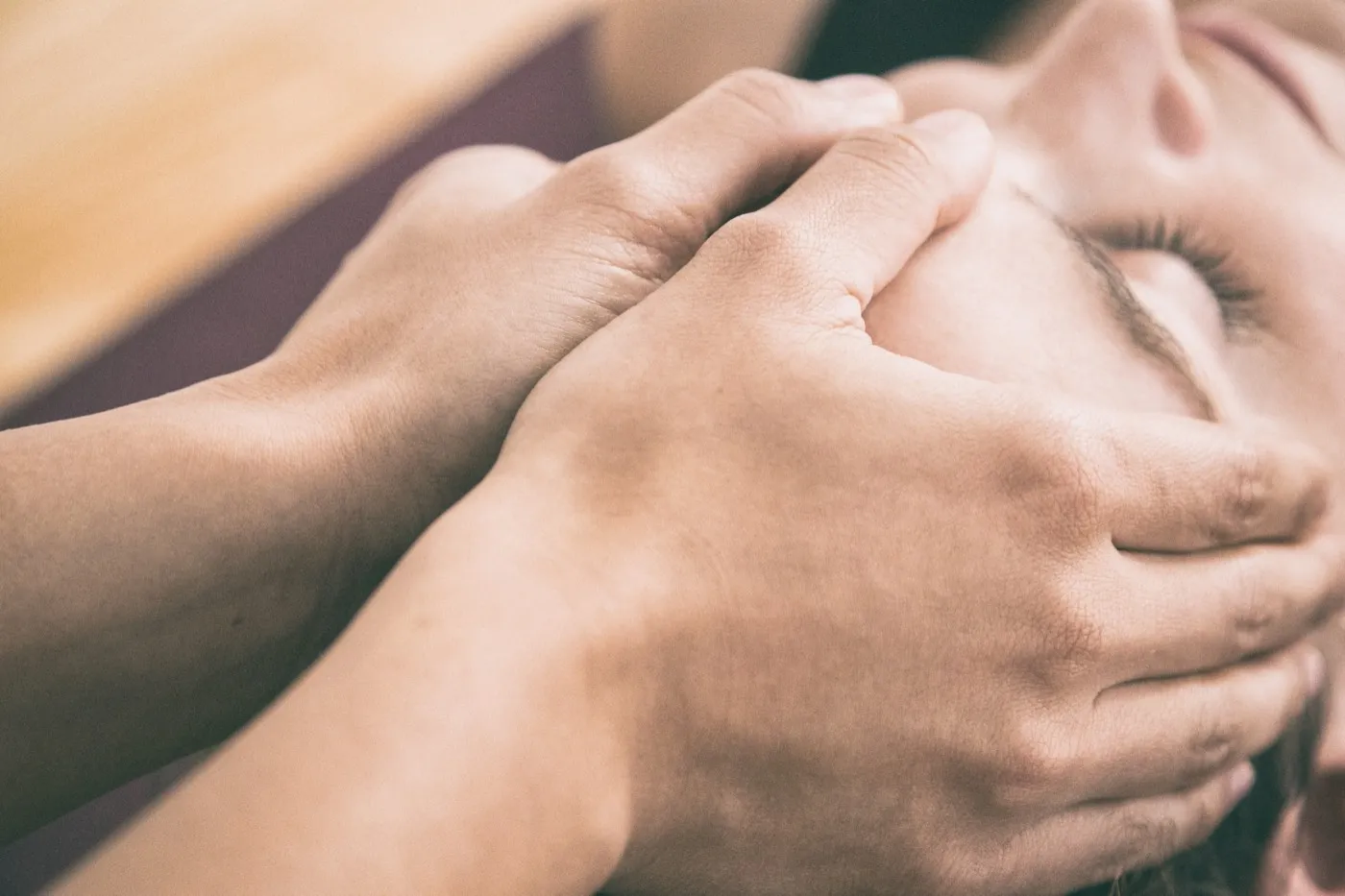 Therapeutin hält mit beiden Händen den Kopf einer entspannt liegenden Frau