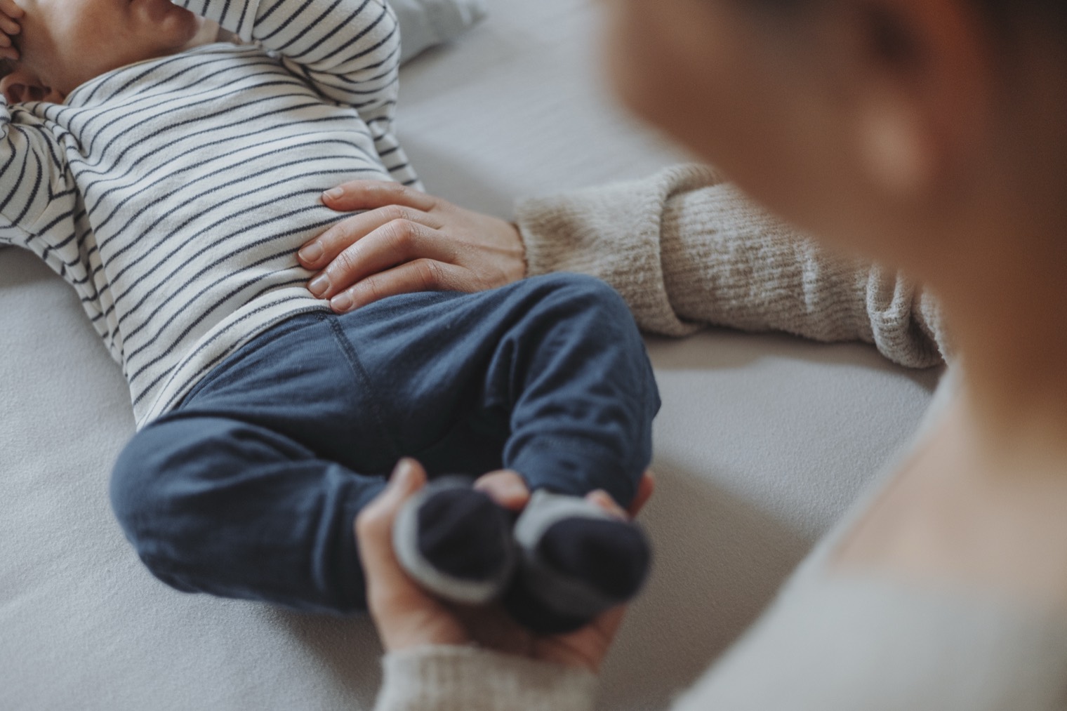 Baby liegt auf der Behandlungsliege, eine Hand ruht sanft auf dem Bauch, die andere hält die Füsschen.
