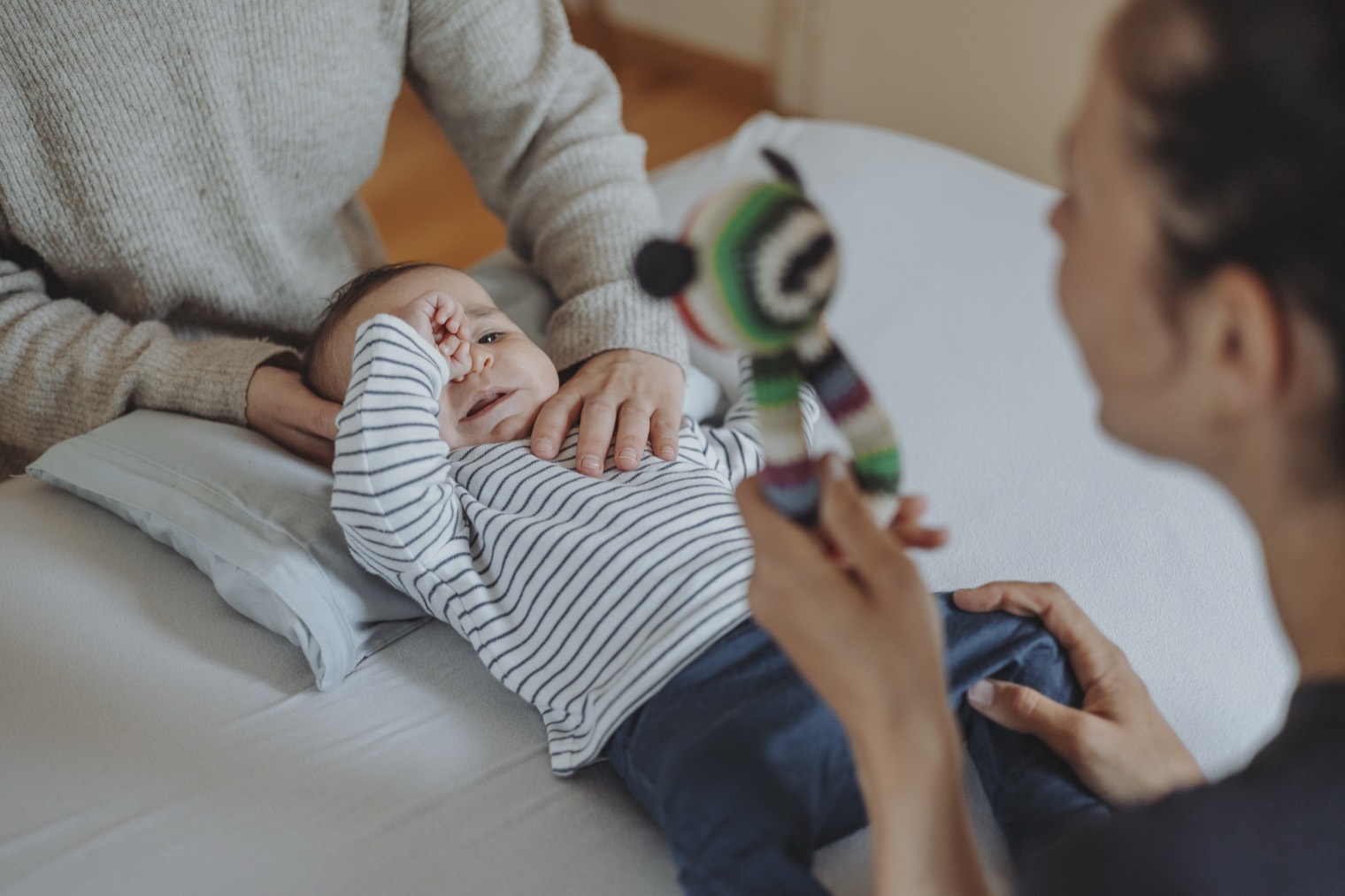 Baby liegt entspannt auf der Behandlungsliege, eine Hand ruht sanft auf seinem Brustkorb, die Mutter ist nah dabei.