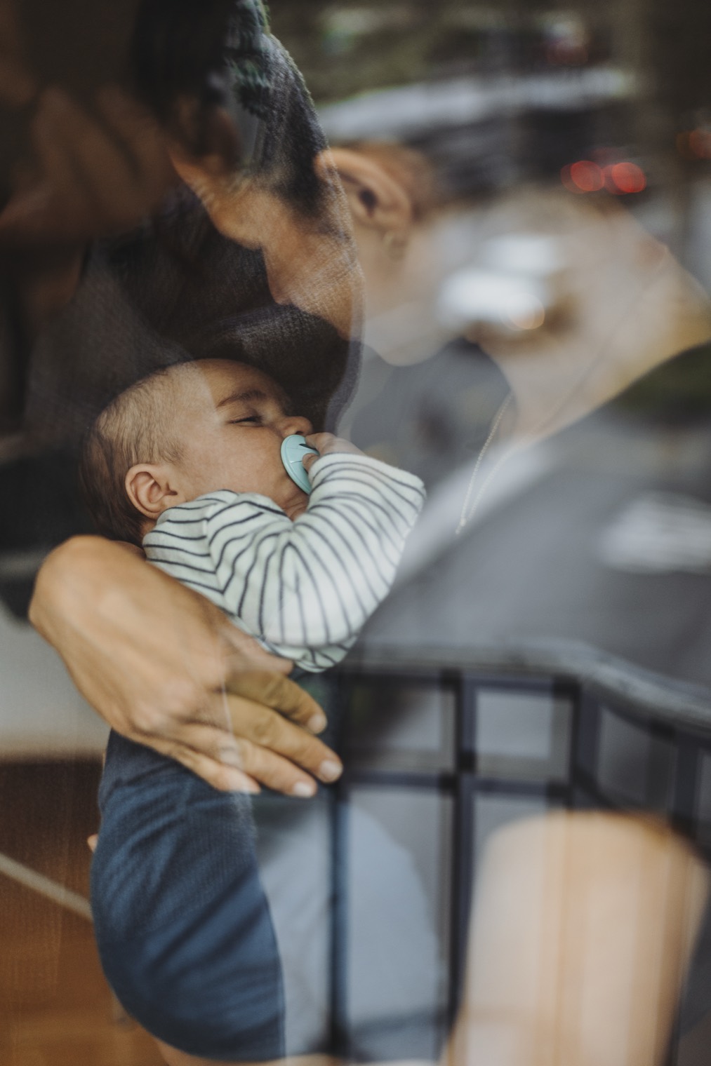 Mutter hält ihr ruhiges Baby im Arm am Fenster.