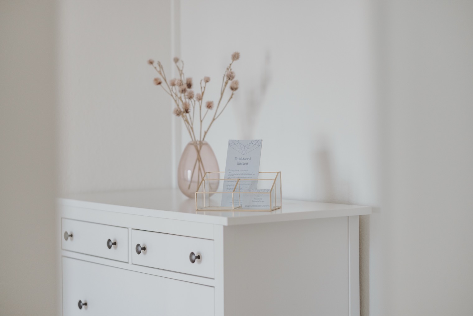 Kommode mit getrockneten Blumen und Informationskarten zur Craniosacral Therapie.